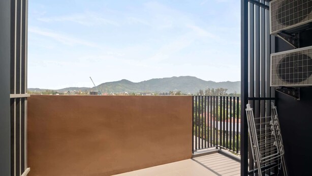 Un balcon offrant une vue sur les montagnes lointaines, un étendoir métallique et une rambarde noire.