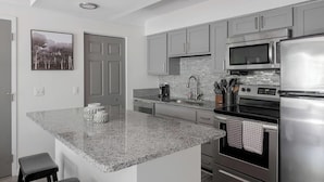 Cozinha moderna com bancadas de granito, eletrodomésticos de aço inoxidável e armários cinzas.