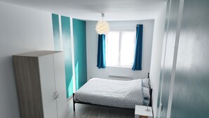 A bedroom with a bed, a wardrobe, a window with curtains, and a hanging light fixture. - Large city apartment with 2 private indoor parking spaces (Beuvrages)