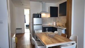 A modern kitchen with white cabinets, a marble backsplash, and a wooden dining table with white chairs. - Large city apartment with 2 private indoor parking spaces (Beuvrages)