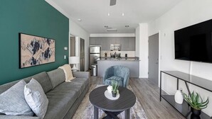 Ein modernes Wohnzimmer mit einem grauen Sofa, einem runden Couchtisch und einem großen Gemälde an der Wand.