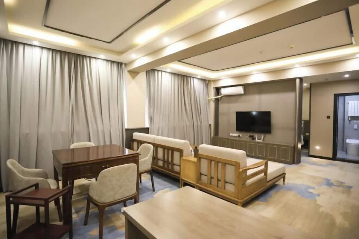 Quarto de hotel com mesa de jantar, cadeiras, sofá, televisão e cortinas.