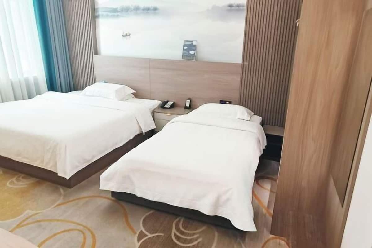 Quarto de hotel com duas camas, cabeceira de madeira, mesa de cabeceira com telefone e vista para a água através da janela.