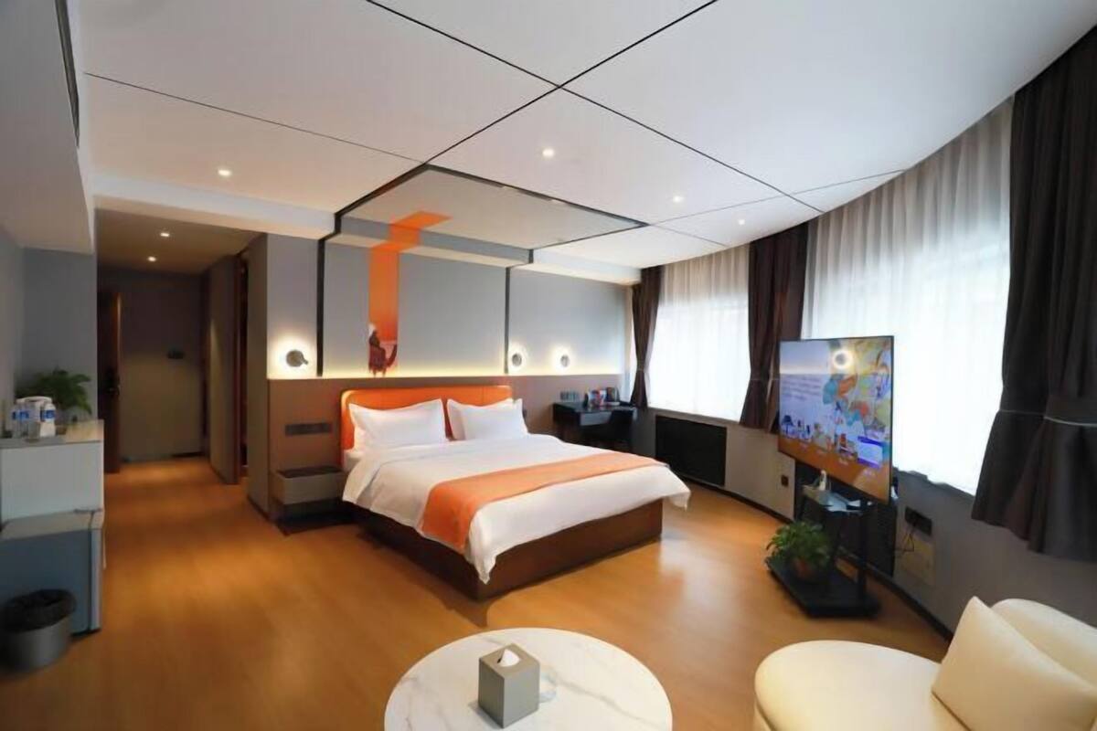 Quarto de hotel moderno com uma cama grande, televisão, escrivaninha e área de estar.