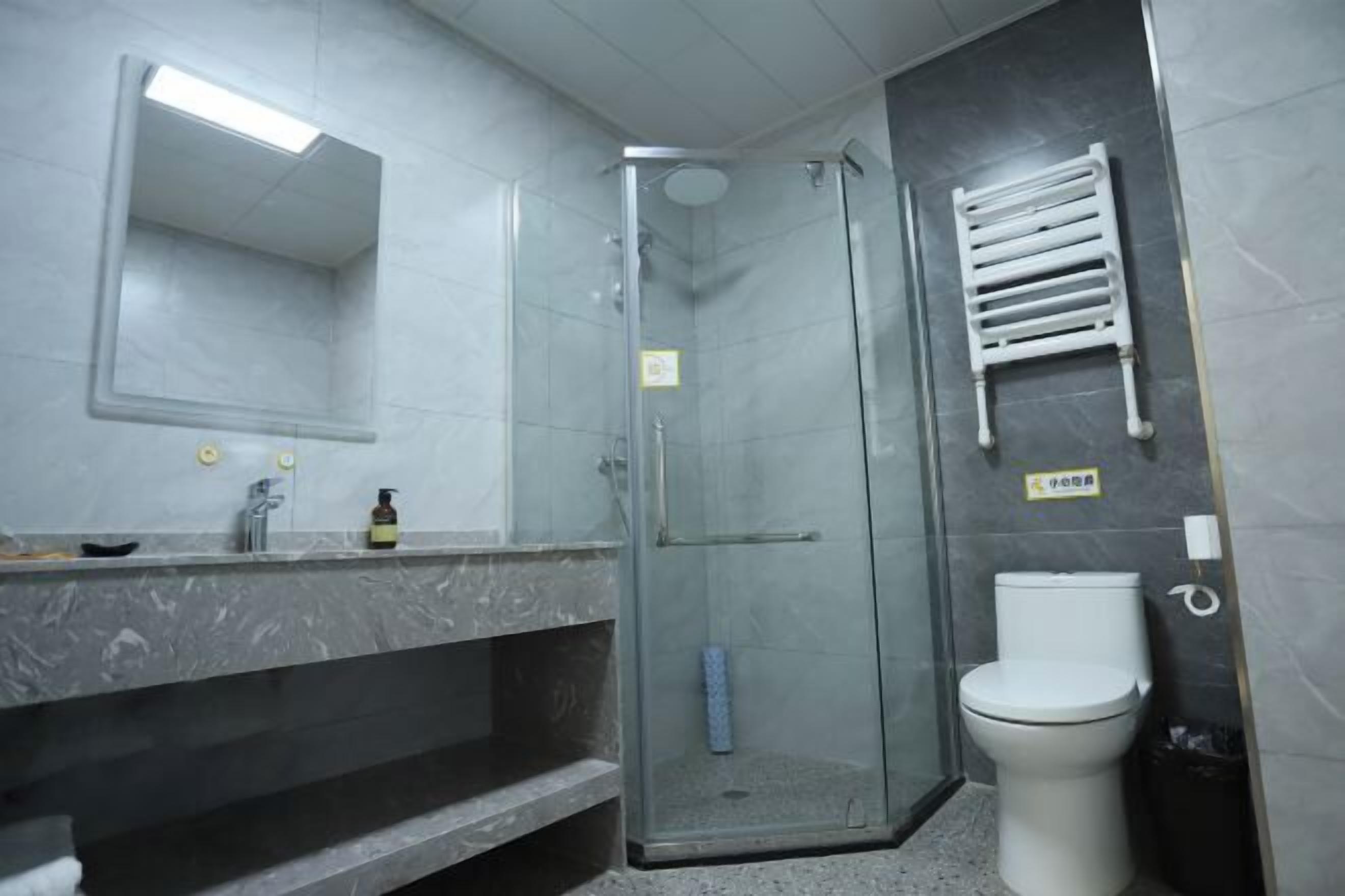 Un baño con ducha de vidrio, inodoro, lavabo con espejo y un perchero para toallas.