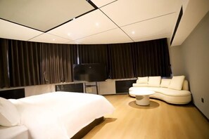 A modern hotel room with a curved bed, a white sofa, a coffee table, and a flat-screen TV. - Peoples Hotel (Lanzhou)