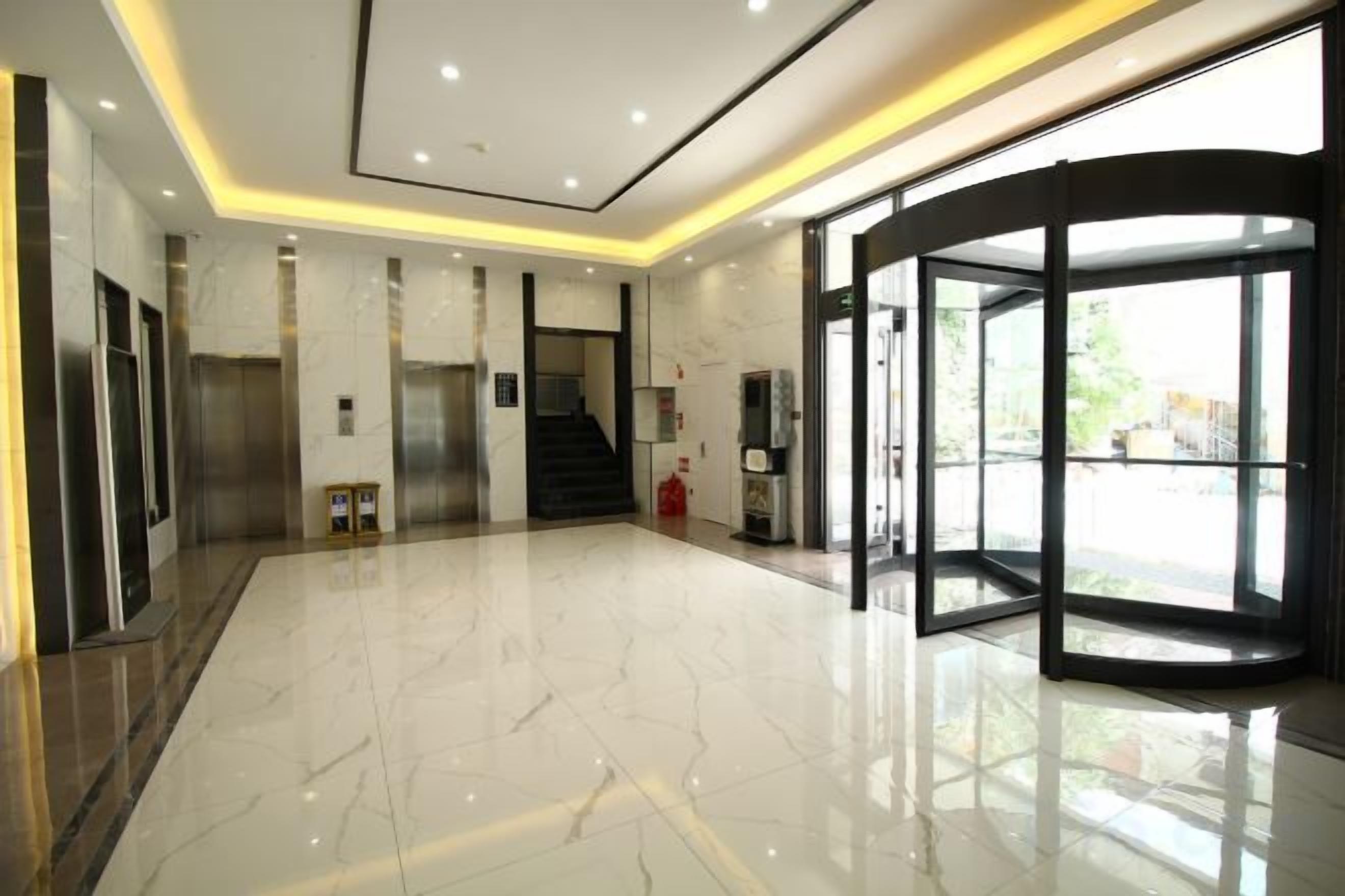 A lobby with a marble floor, elevators, a staircase, and a revolving door.