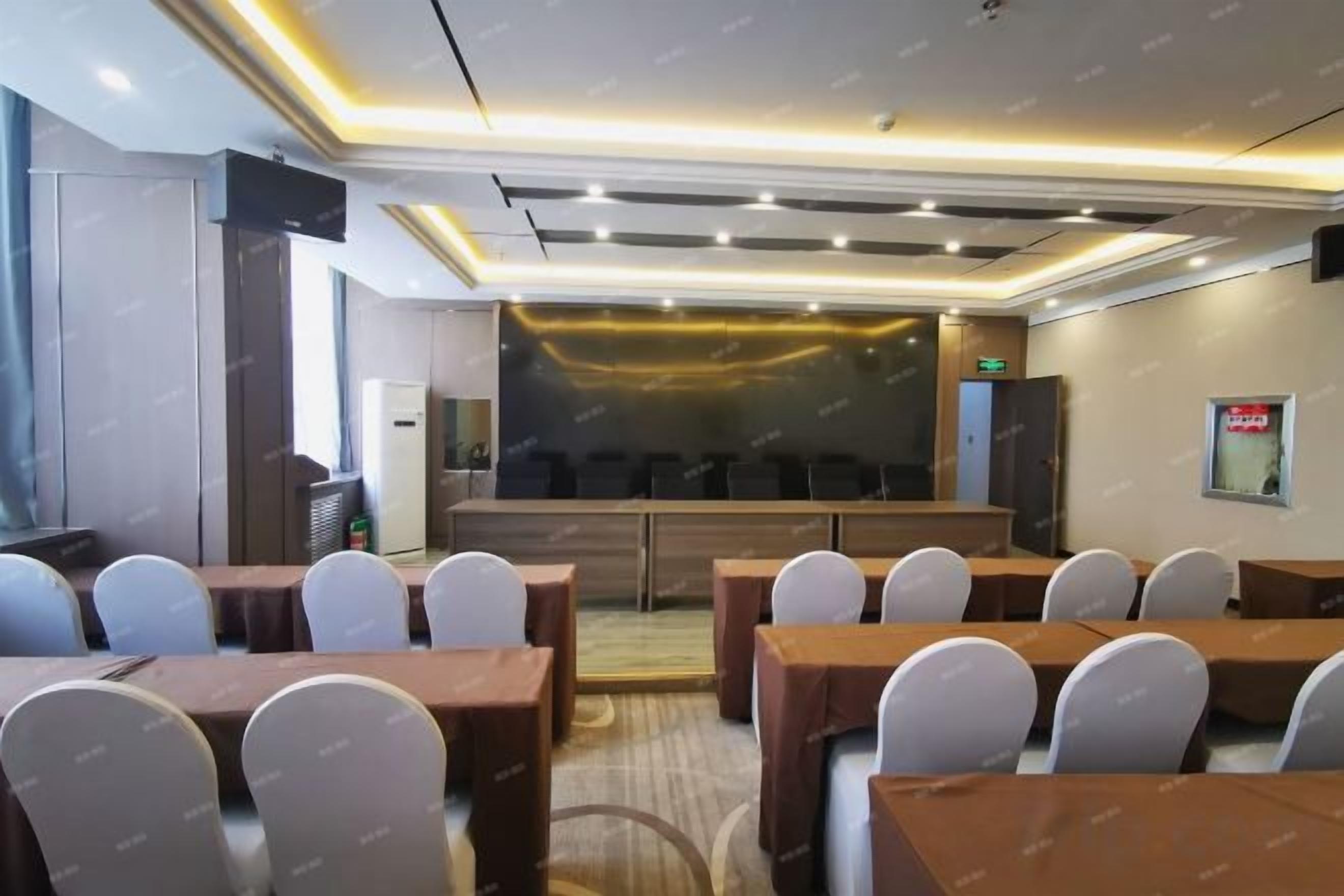 A conference room with multiple tables and chairs, a stage, and a large screen.