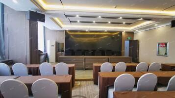 A conference room with multiple tables and chairs, a stage, and a large screen.