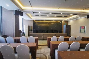 A conference room with multiple tables and chairs, a stage, and a large screen.