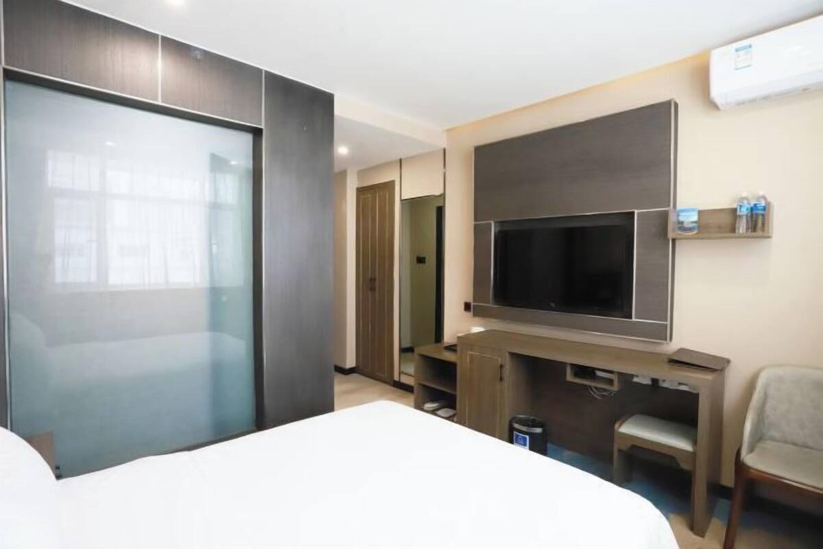 Quarto de hotel com cama, televisão na parede, escrivaninha com cadeira e guarda-roupa.