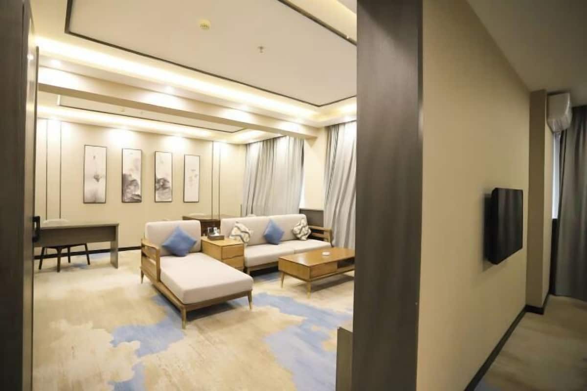 Quarto de hotel moderno com um sofá, uma mesa de centro, uma TV fixada na parede e obras de arte nas paredes.