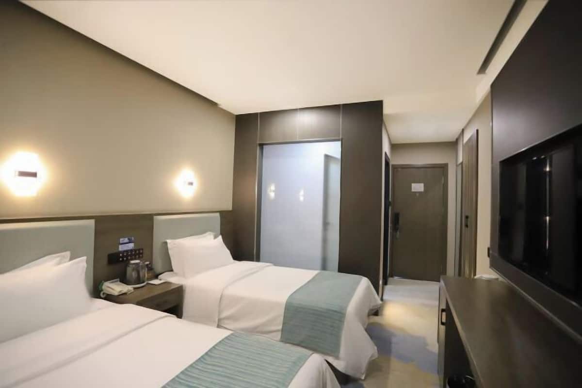 Quarto de hotel com duas camas, televisão, minibar e porta que dá para um corredor.