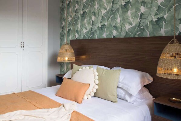 A neatly made bed with a white and orange blanket, surrounded by pillows in various colors and textures.