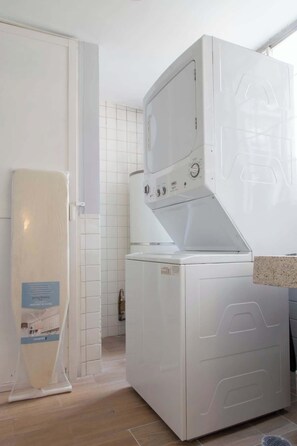 A compact laundry room with a front-loading washer and dryer, a tiled backsplash, and a wooden floor.