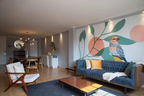 A modern living room with a blue sofa, wooden coffee table, and a dining area with a wooden table and chairs.