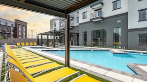 Ein modernes Gebäude mit Schwimmbad, gelben Liegestühlen und einem überdachten Sitzbereich.