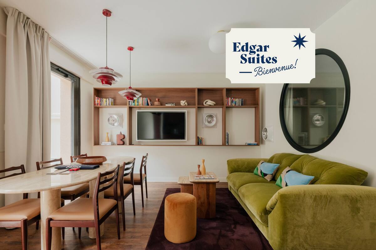 Een moderne woonkamer met een groene bank, een houten eettafel en een aan de muur bevestigde televisie.