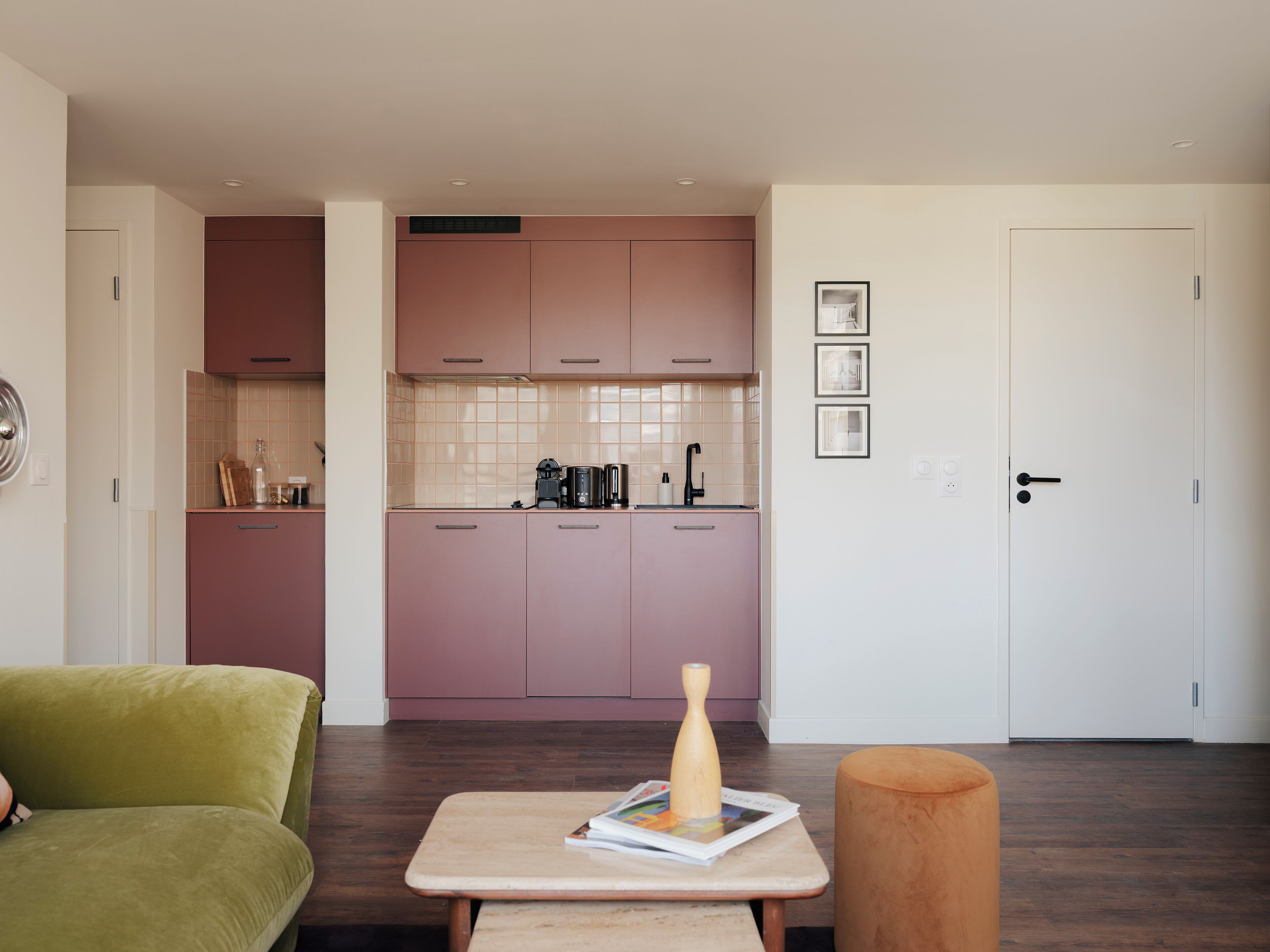 A modern kitchen with pink cabinets, a white door, and a small table with a magazine.