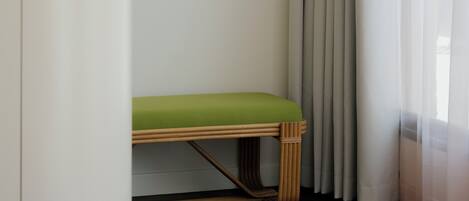 A room with a wooden bench, a framed abstract painting, and a window with sheer curtains.