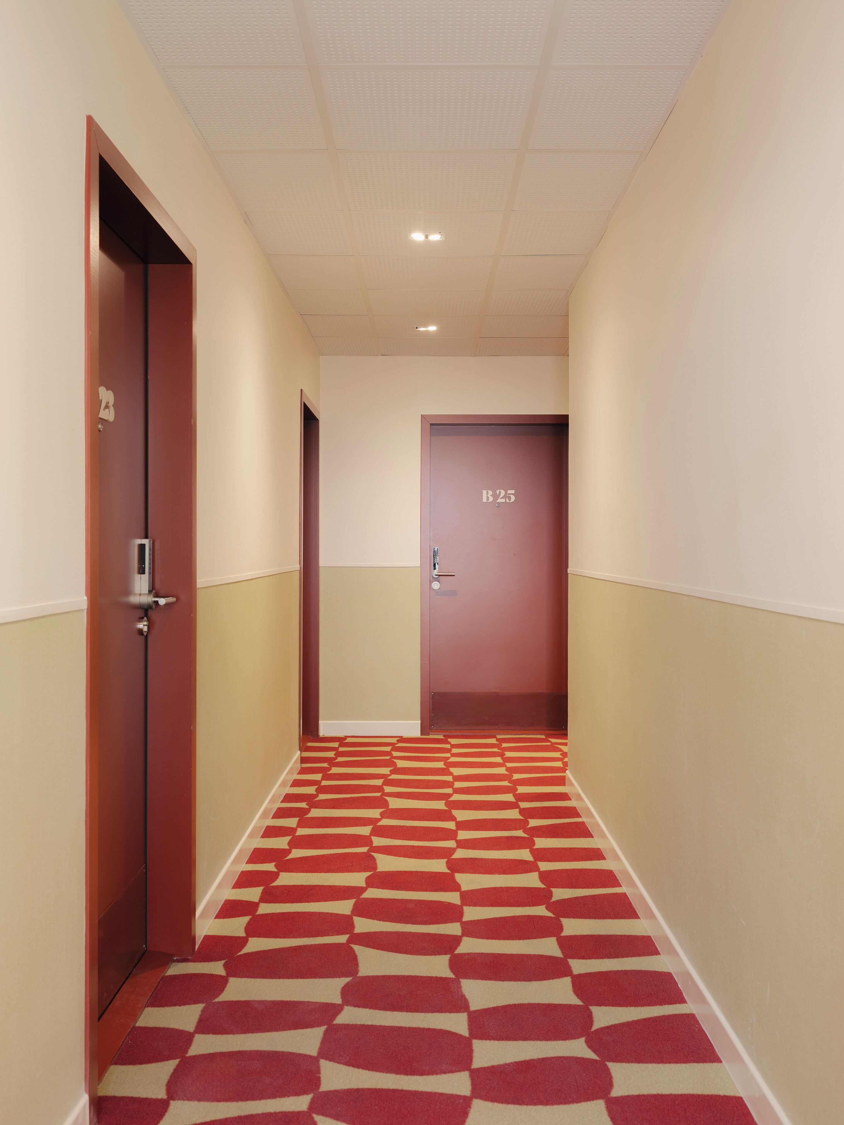 A hallway with a patterned carpet, a door labeled "B25", and a ceiling with recessed lighting.