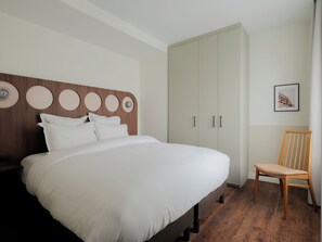 A neatly made bed with white linens, a wooden headboard with circular decorations, a large wardrobe, and a wooden chair. - Edgar Suites Levallois - Anatole France (Levallois-Perret)
