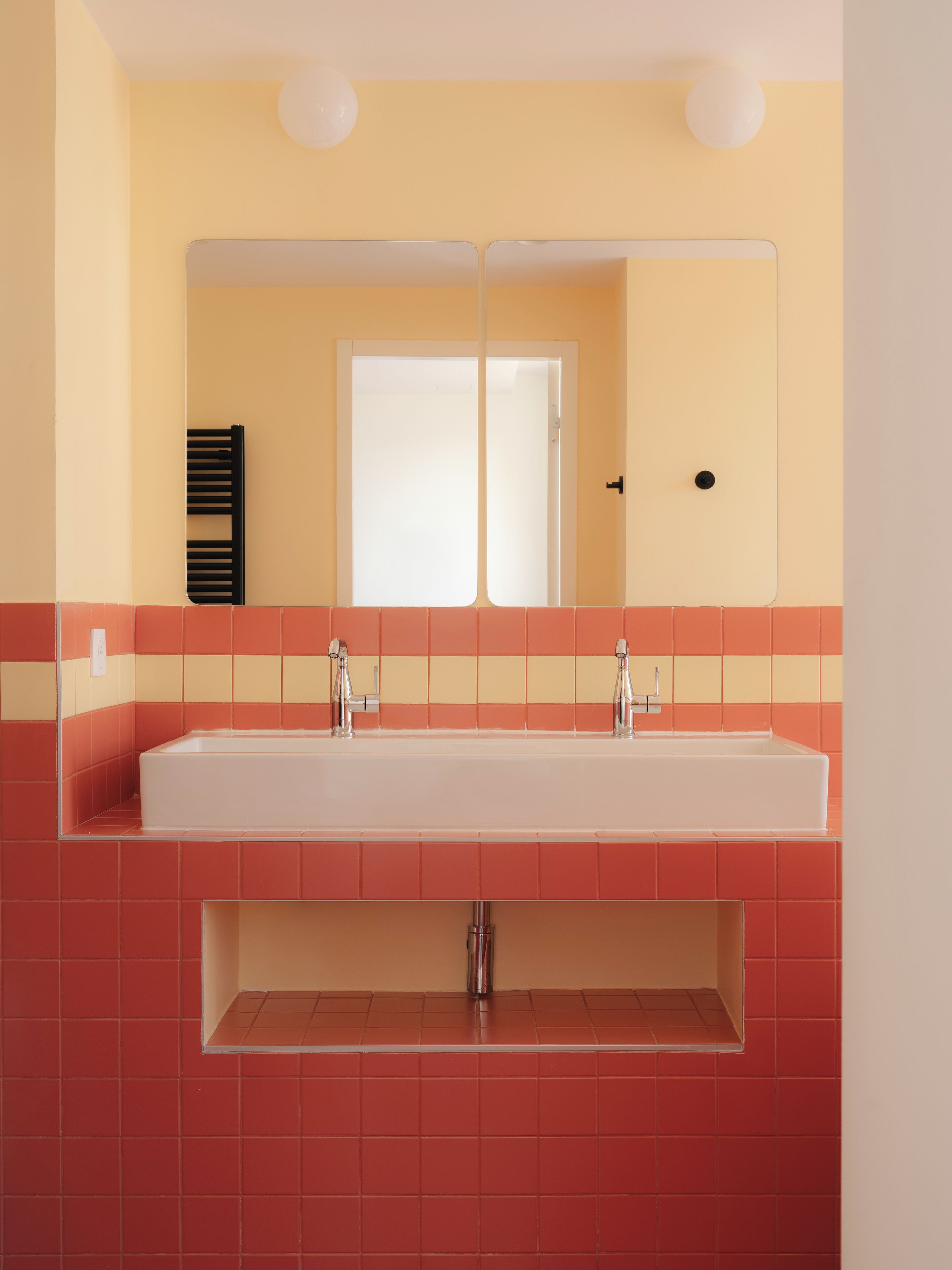 A bathroom with a white sink, two mirrors, and red and yellow tiles.