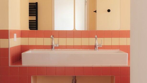 Casa de banho com uma pia branca, dois espelhos e azulejos vermelhos e amarelos.