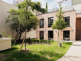 A modern building with numbered doors, a grassy courtyard, and trees.