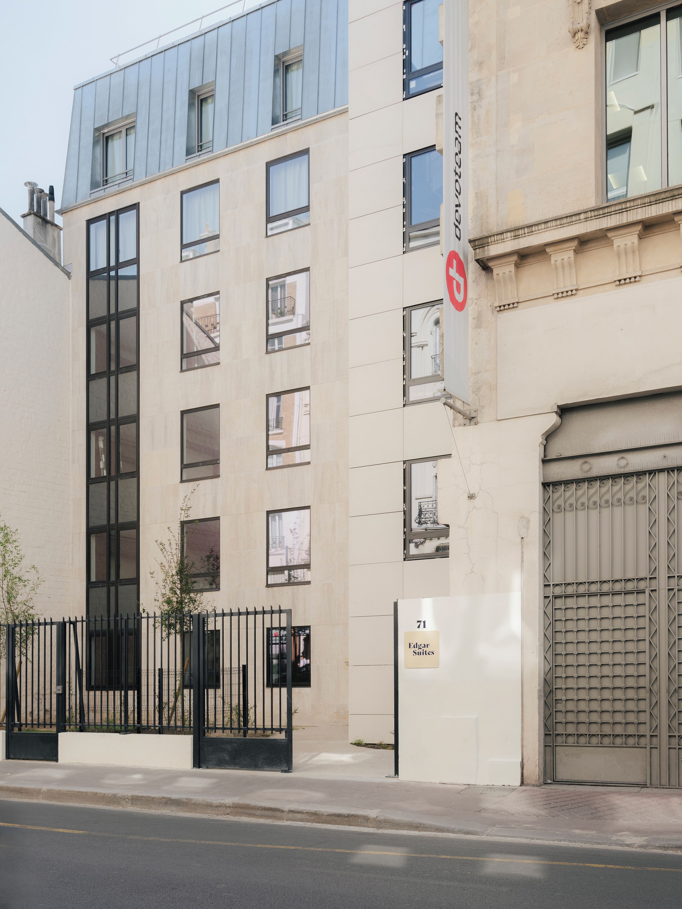 A modern building with a beige facade, large windows, and a gated entrance.