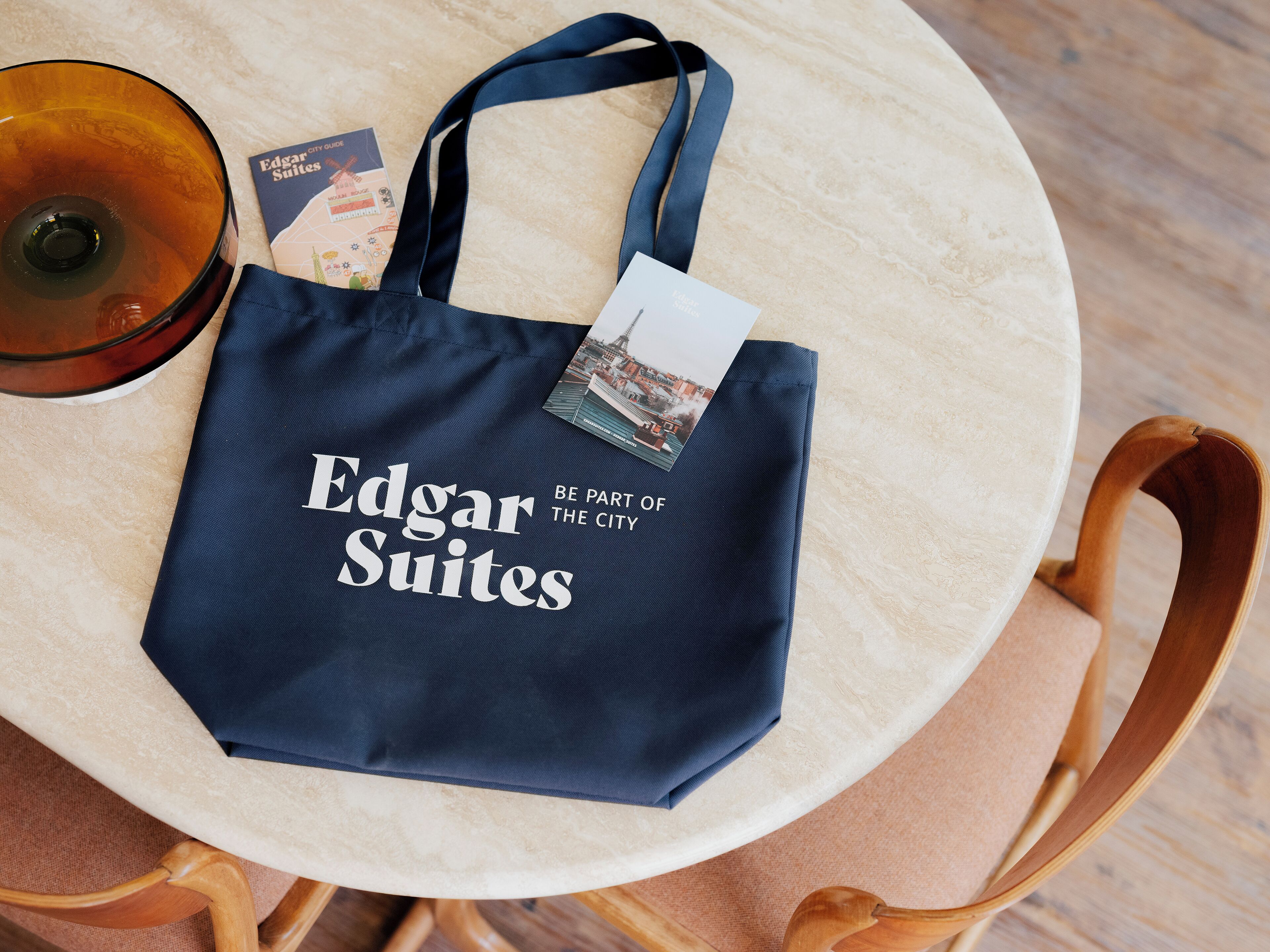 Eine dunkelblaue Tragetasche mit dem Aufdruck "Edgar Suites" und "Sei Teil der Stadt", platziert auf einem runden Tisch.