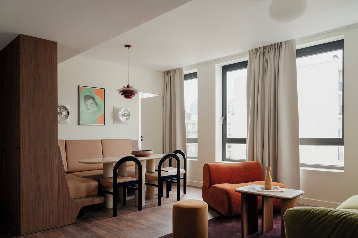 Een moderne woonkamer met een bank, stoelen, een tafel en een groot raam met gordijnen.