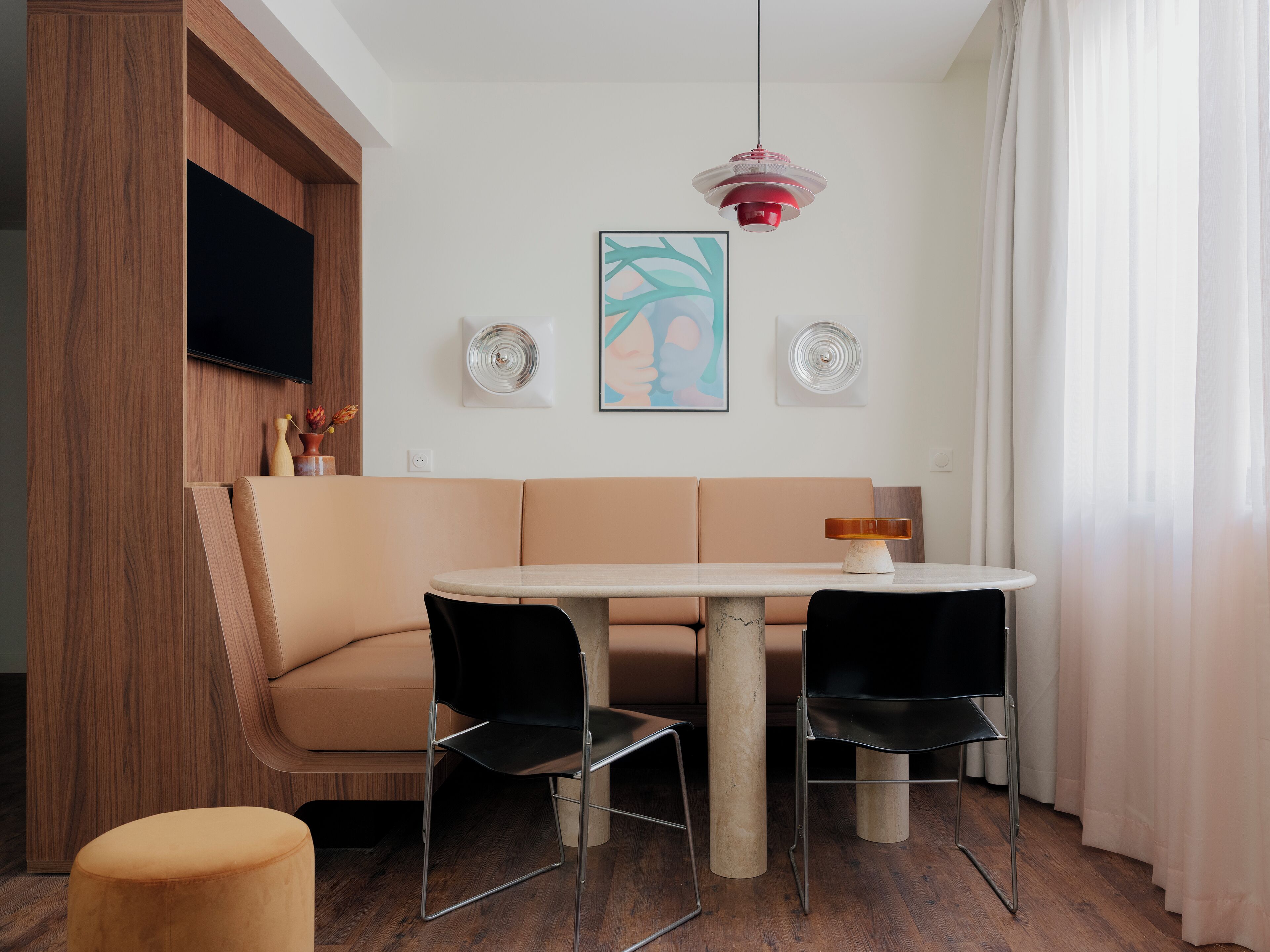 Un comedor moderno con una mesa redonda, dos sillas negras, un sofá beige y una lámpara colgante roja.