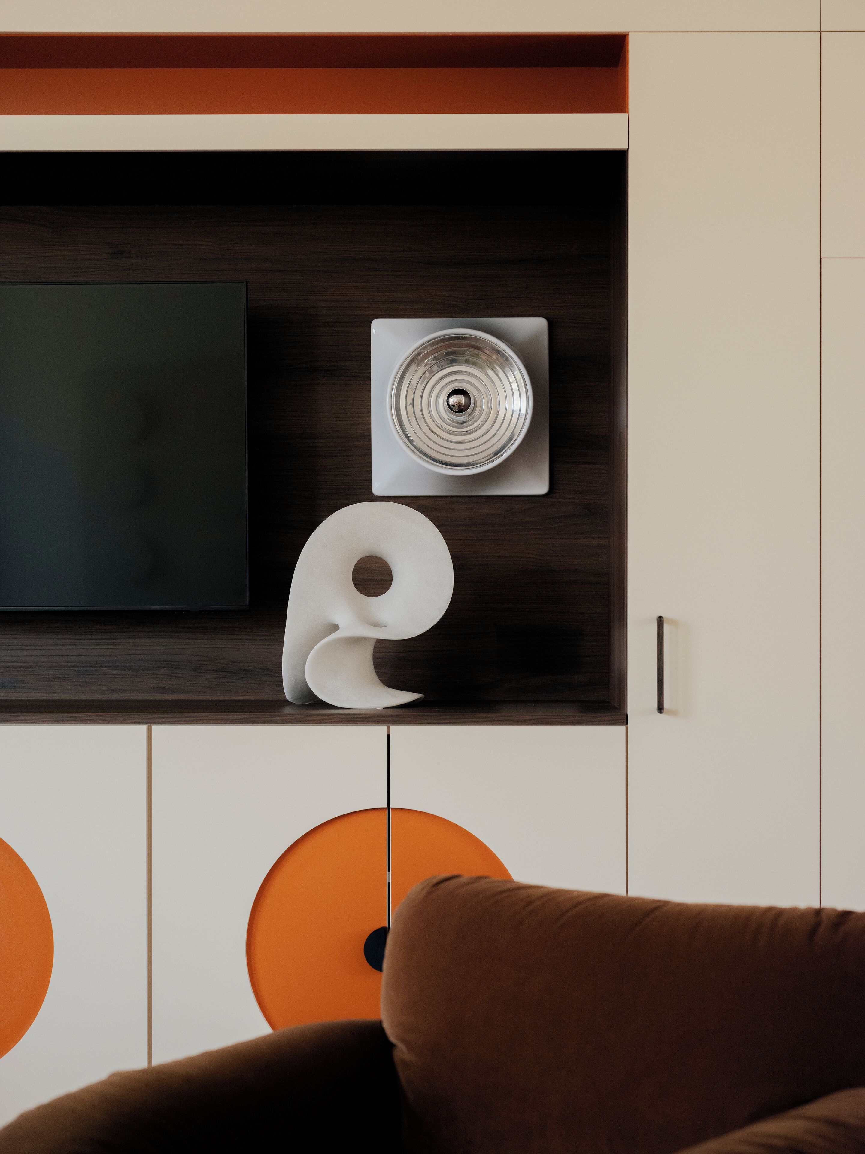 A modern living room with a flat-screen TV, a decorative wall piece, and a brown sofa.