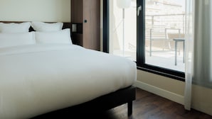 A hotel room with a large bed, wooden headboard, and a balcony with a view of buildings.
