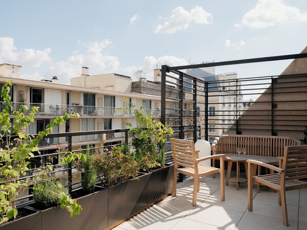 A rooftop terrace with wooden furniture, potted plants, and a view of neighboring buildings. - Edgar Suites Levallois - Anatole France (Levallois-Perret)