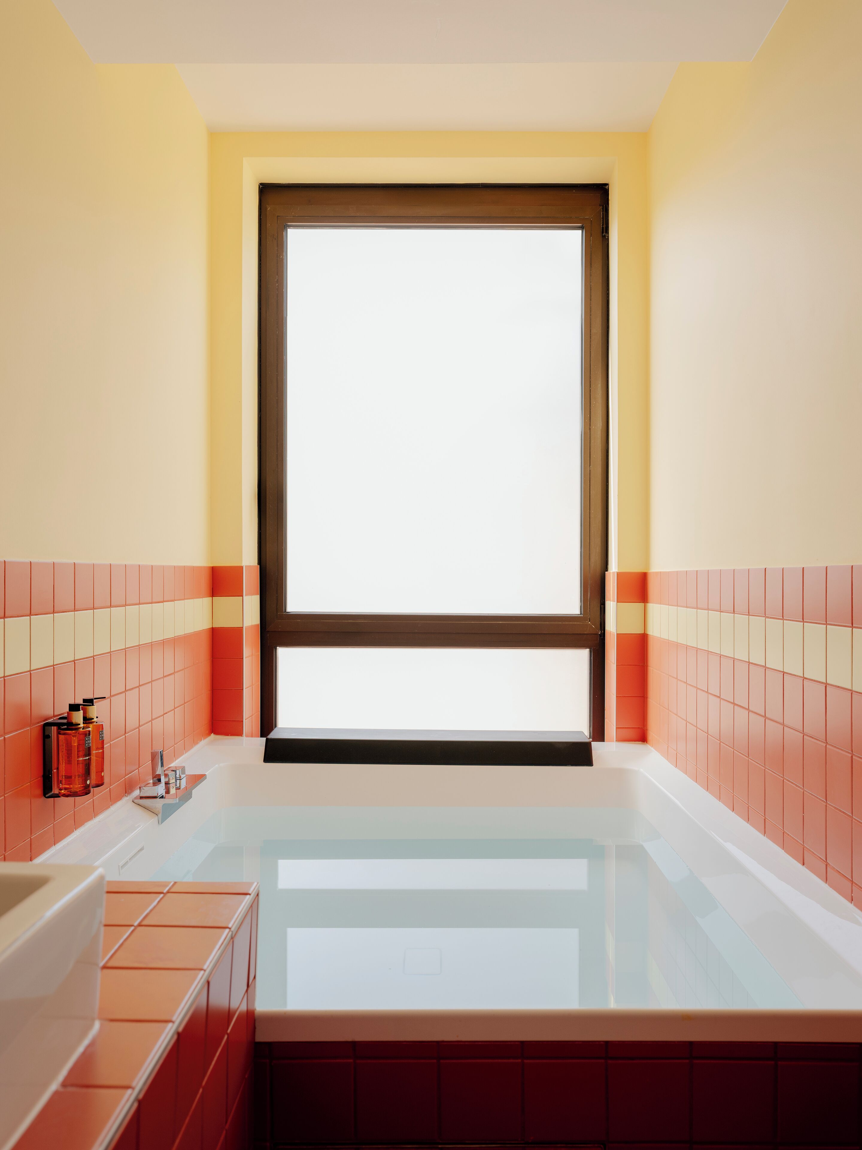 A bathroom with a bathtub, a window, and tiled walls.