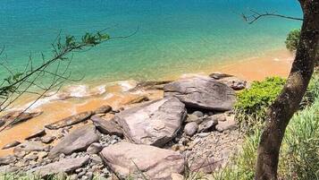 A beach with clear turquoise water, rocky shoreline, and lush greenery.