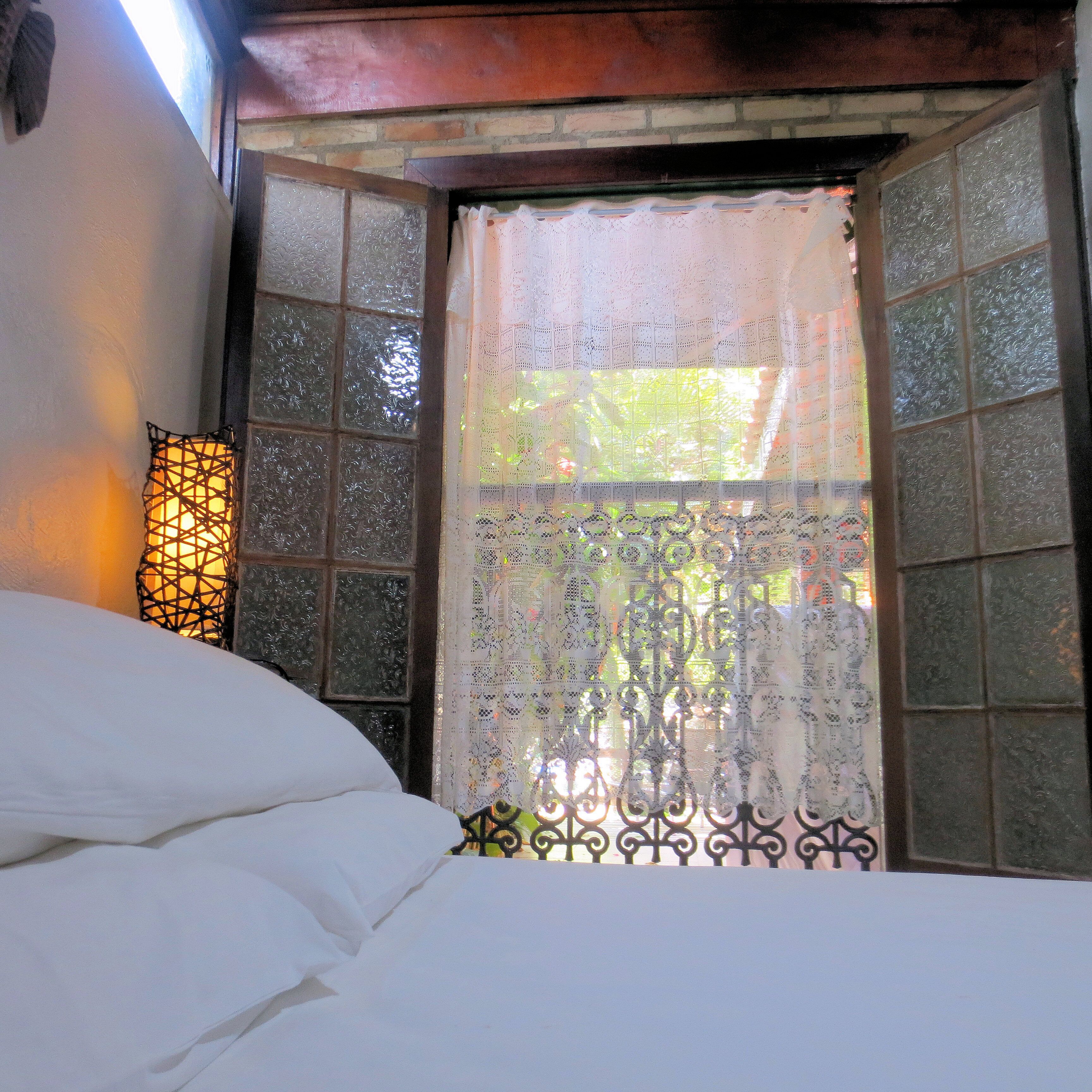 A room with a bed, a window with decorative glass panes, and a wall-mounted light fixture.