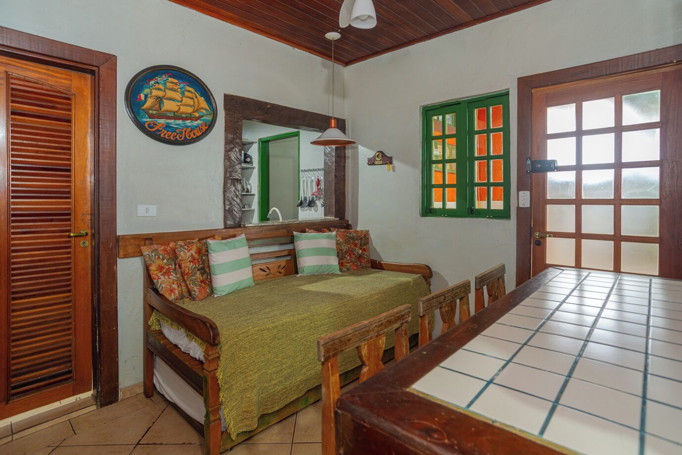 A room with a wooden sofa, a dining table, a green door, and a wall-mounted clock.