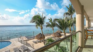 A balcony with a view of a beach, palm trees, and a pool.