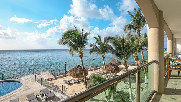 Un balcón con vista a una playa, palmeras y una piscina.