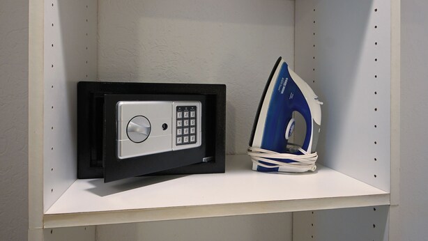 A security safe and an iron on a white shelf.