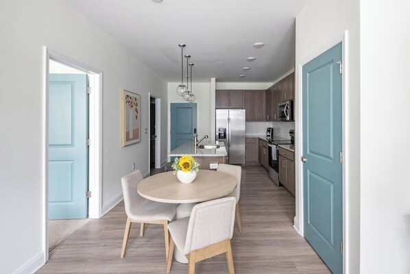 A modern kitchen with stainless steel appliances, a dining area with a round table and chairs, and light blue doors.