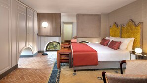 A hotel room with a large bed, a red accent wall, a patterned rug, and a view of greenery through a window.