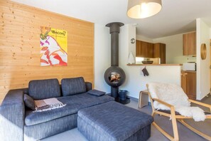 Ein modernes Wohnzimmer mit einem grauen Ecksofa, einem runden Kaminofen und einer Holzvertäfelung.