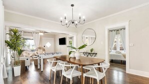 Un salón amplio con una mesa de comedor de madera, sillas blancas, una mesa de fútbol y una araña.
