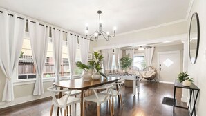 Un comedor amplio con una mesa de madera y sillas blancas, un candelabro y plantas en macetas.