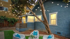 Patio con una casa azul, un árbol y mobiliario exterior.