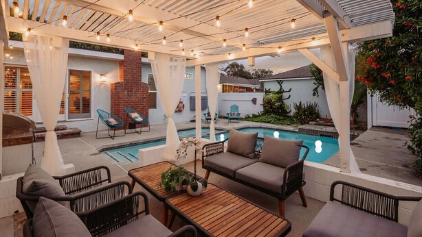 Un patio exterior con piscina, muebles de madera y luces colgantes.